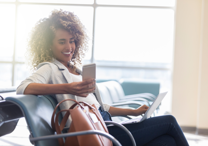 A person sitting at an airport working on her laptop and phone
