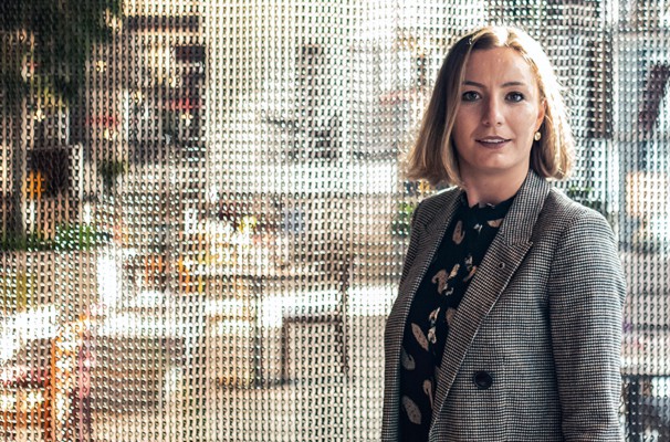 In a light and modern hotel lounge area. A young woman in a business outfit is looking directly into the camera.