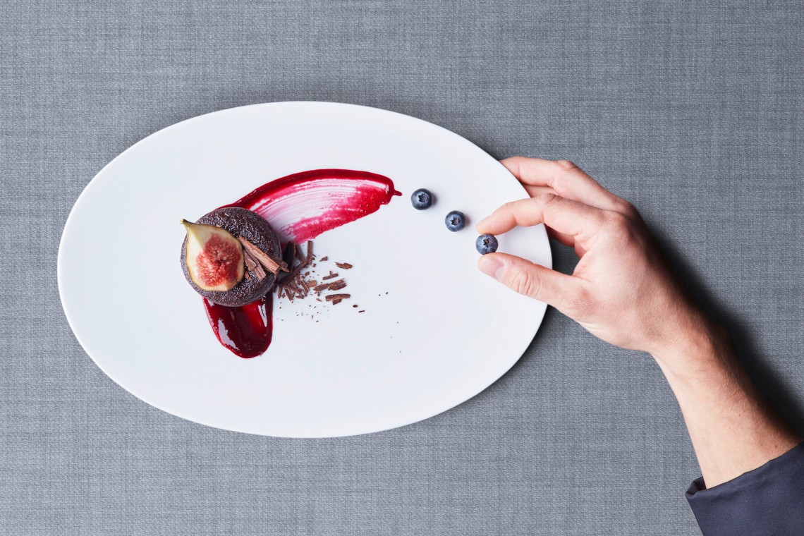 Close-up on a hand that is artfully arranging food on a plate.